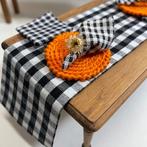 Könnte beinhalten: Ein schwarz-weiß karierter Tischläufer mit orangefarbenen gehäkelten Platzsets und einer schwarz-weiß karierten Serviette mit Sonnenblumen-Akzent.