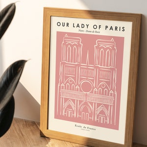 May include: A framed print with a pink background and a white line drawing of Notre Dame Cathedral in Paris. The text "Our Lady of Paris" is at the top of the print, and the text "Notre Dame de Paris" is below the drawing. The text "Ecole de France 1163-1345" is at the bottom of the print.