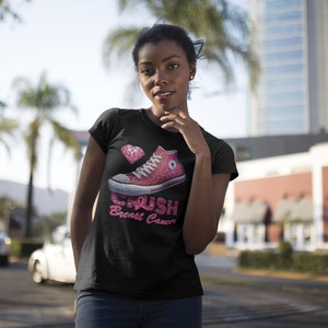May include: Black t-shirt featuring a pink high-top sneaker design with the words "Crush Breast Cancer." A pink diamond graphic is also present. The shirt is a classic crew neck style.