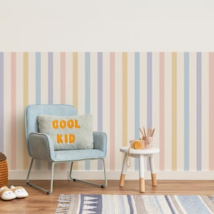 May include: A child's room with a light blue chair, a small white table, and a striped rug. The chair has a pillow with the words "COOL KID" in orange. The wall has vertical stripes in pastel colors.