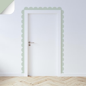 Puede incluir: Una puerta blanca con manija y cerradura plateadas está enmarcada por un borde festoneado en un color verde suave. La puerta está colocada contra una pared blanca, con una sección de la pared que se desprende para revelar el mismo color verde. El suelo es de madera clara.