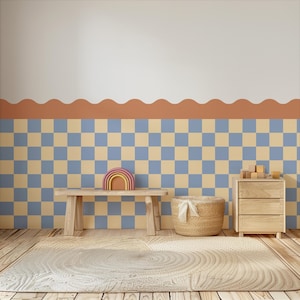 Op de afbeelding: Een kinderkamer met een houten bank, een regenboogvormig speelgoed en een rieten mand. De muur heeft een dambordpatroon in blauw en beige, met een geschulpte rand. Een houten ladekast en een rond tapijt maken de scène compleet.