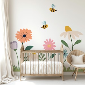 May include: A nursery scene featuring a wooden crib, a wicker chair with a white pillow, and a wall decorated with large, colorful flower and bee decals. The flowers are in shades of orange, pink, purple, and white, with green leaves and grass.
