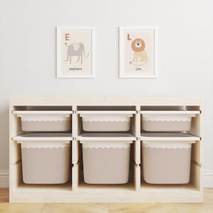 May include: A light wood storage unit with six compartments, each holding a beige bin with a scalloped edge. Two framed animal alphabet prints hang above. One shows an elephant, the other a lion.
