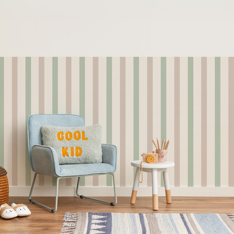 May include: A child's room with a light blue chair, a small white table, and a striped wallpaper in beige, green, and brown. A pillow with the words "COOL KID" is on the chair. A rug and a small toy camera are also visible.