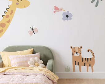 Op de afbeelding: Een set muurstickers met een gele giraf, een bruine tijger, een roze vogel, een lichtpaarse bloem, een roze vlinder en groene bladeren. De stickers zijn op een effen muur geplaatst boven een bed met een groen frame en roze beddengoed.