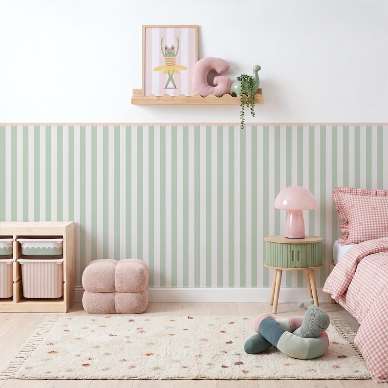 May include: A bedroom featuring sage green and white striped wallpaper, a light wood shelf with a frog print, a pink letter G pillow, and a green dinosaur. Includes a light wood storage unit, a pink mushroom lamp, and a pink gingham bed.