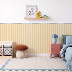 May include: Wallpaper featuring vertical yellow and white stripes with a blue scalloped border at the top. The design creates a clean, repetitive pattern suitable for wall decor, providing a bright and structured aesthetic for a room interior.