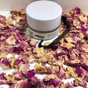 Pu&ograve; includere: Un piccolo barattolo bianco con un coperchio beige che contiene un prodotto di bellezza naturale. Il barattolo &egrave; etichettato "blk natural beauty & kindness". Il barattolo &egrave; circondato da petali di rosa secchi e una bacca di vaniglia.