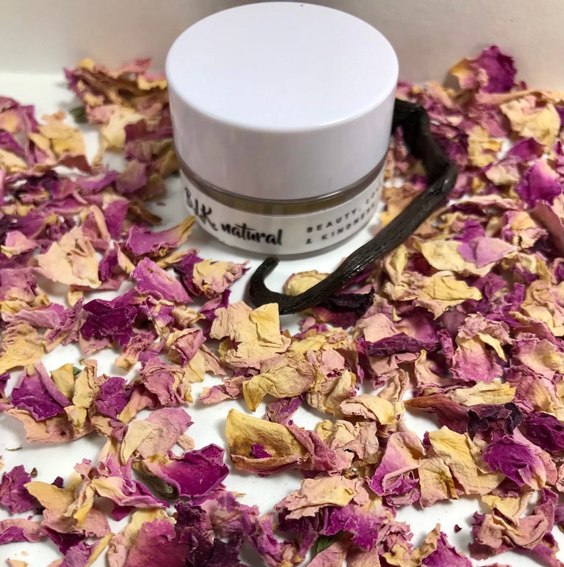 Pu&ograve; includere: Un piccolo barattolo bianco con un coperchio beige che contiene un prodotto di bellezza naturale. Il barattolo &egrave; etichettato "blk natural beauty & kindness". Il barattolo &egrave; circondato da petali di rosa secchi e una bacca di vaniglia.