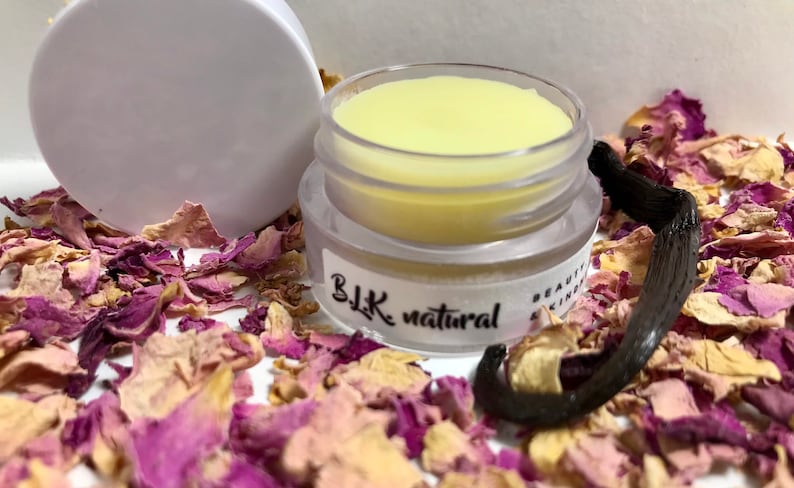 Pu&ograve; includere: Un piccolo barattolo trasparente con un balsamo per labbra giallo al suo interno. Il barattolo ha un'etichetta nera che recita "BLK natural". Il barattolo &egrave; circondato da petali di rosa secchi e una bacca di vaniglia.
