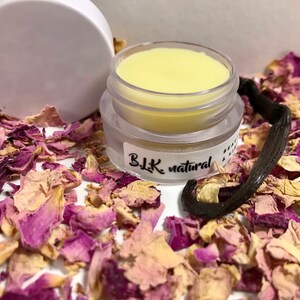 Pu&ograve; includere: Un piccolo barattolo trasparente di balsamo per labbra giallo con un coperchio bianco. Il barattolo &egrave; etichettato "BLK natural" ed &egrave; circondato da petali di rosa secchi e un baccello di vaniglia.