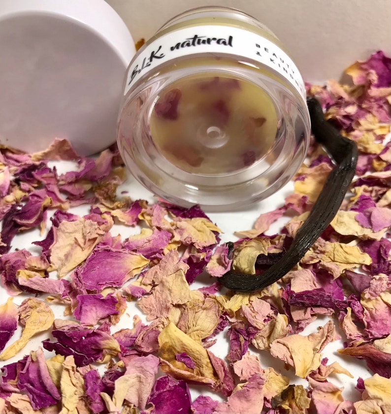 Pu&ograve; includere: Un barattolo di vetro trasparente con un coperchio bianco riempito di un balsamo giallo chiaro. Il barattolo ha un'etichetta nera su cui &egrave; scritto "BLK natural". Il barattolo &egrave; circondato da petali di rosa secchi e una bacca di vaniglia.