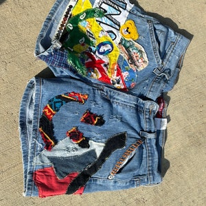 Könnte beinhalten: Blaue Jeans-Shorts mit bunten Patches und Stickereien. Die Patches beinhalten ein Smiley, einen Teddybär und eine Vielzahl anderer Designs.