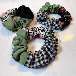 Könnte beinhalten: Drei Stoff-Haargummis in verschiedenen Mustern und Farben. Eines hat schwarzen Samt, ein anderes einen Blumendruck und das dritte ein schwarz-weißes Vichy-Muster. Die Haargummis sind ein Haaraccessoire.