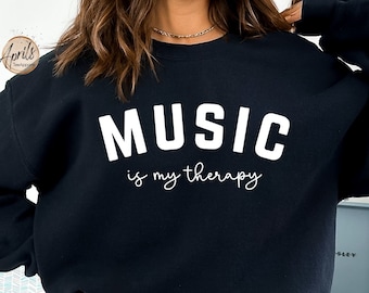 Pode incluir: Camisola de moletom preta com texto branco que diz "MUSIC is my therapy".