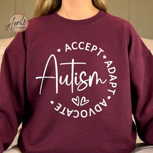 May include: A maroon sweatshirt with a white circle graphic that says "Accept, Autism, Adapt, Advocate" with two hearts in the center.