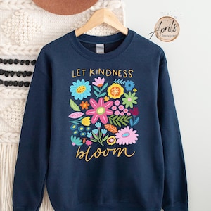 May include: Navy blue sweatshirt with a colorful floral design and the text "Let Kindness Bloom" in gold lettering.