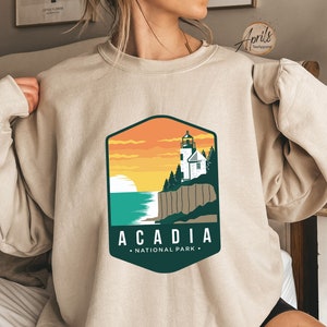 K&ouml;nnte beinhalten: Ein beiger Pullover mit einem grafischen Design eines Leuchtturms und dem Text "Acadia National Park".