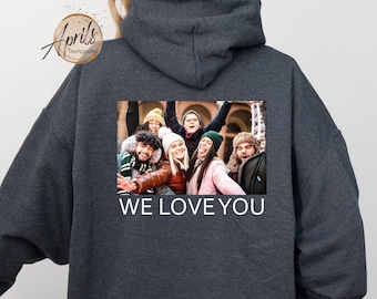 Może przedstawiać: Szara bluza z kapturem z nadrukiem zdjęcia grupy uśmiechniętych osób i tekstem "WE LOVE YOU" na plecach.