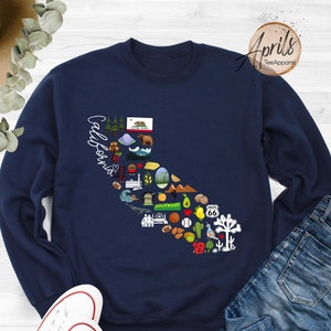 May include: A navy blue sweatshirt with a graphic of the state of California, featuring various icons representing the state's culture and landmarks. The text "California" is written in a cursive font on the left side of the graphic.