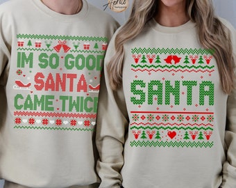 May include: Two beige Christmas sweaters with a green and red pixelated design. One sweater says "I'm so good Santa came twice" and the other says "Santa".