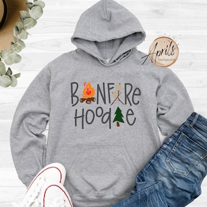 May include: Gray hooded sweatshirt with the text "Bonfire Hoodie" in black with a campfire, marshmallows, and a pine tree graphic.