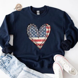 Puede incluir: Una sudadera azul marino con un dise&ntilde;o de coraz&oacute;n de bandera estadounidense desgastado.