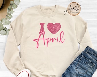 May include: A beige sweatshirt with a pink glitter heart and the text "I love April" printed on the front.