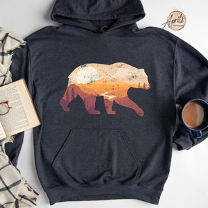 May include: A dark gray hooded sweatshirt with a graphic print of a bear silhouette. The bear is filled with a sunset landscape with orange, yellow, and brown colors.