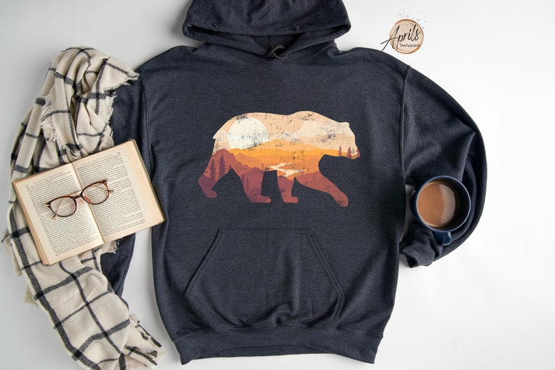 May include: A dark gray hooded sweatshirt with a graphic print of a bear silhouette. The bear is filled with a sunset landscape with orange, yellow, and brown colors.