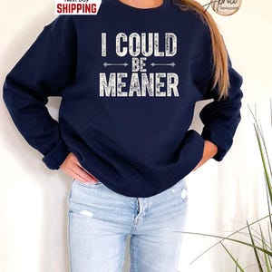 May include: A navy blue sweatshirt with the text "I could be meaner" in white distressed lettering. The text is surrounded by two arrows pointing in opposite directions.