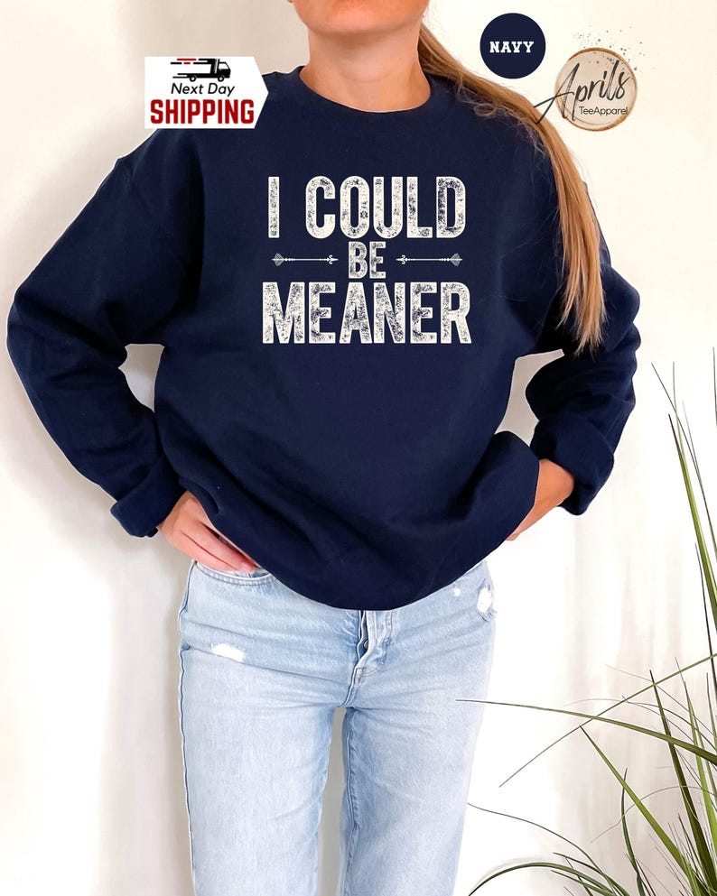 May include: A navy blue sweatshirt with the text "I could be meaner" in white distressed lettering. The text is surrounded by two arrows pointing in opposite directions.