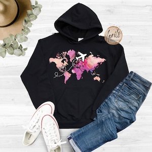 May include: Black hoodie with a watercolor world map design and a white airplane flying over it. The map is in shades of pink, orange, and yellow. The text "Aprils TeeApparel" is in the top right corner.