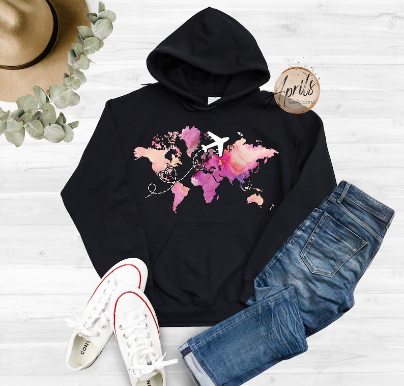 May include: Black hoodie with a watercolor world map design and a white airplane flying over it. The map is in shades of pink, orange, and yellow. The text "Aprils TeeApparel" is in the top right corner.