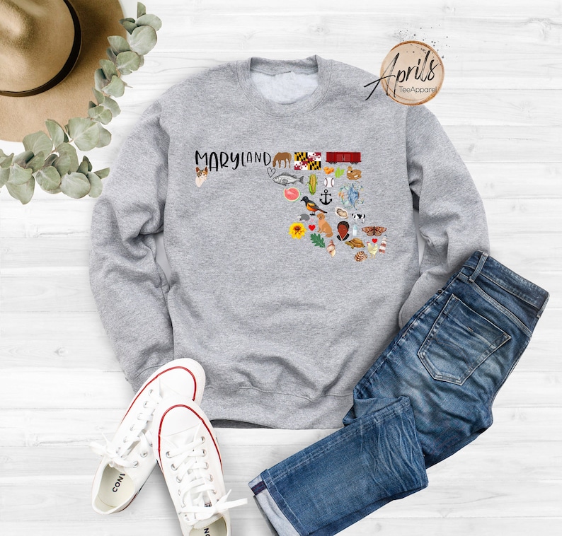 May include: Gray sweatshirt with a graphic of the state of Maryland, featuring various icons representing the state, including a crab, a lighthouse, and a sunflower. The text "MARYLAND" is printed above the graphic.