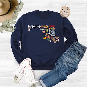 May include: Navy blue sweatshirt with a graphic of the state of Maryland, featuring various icons representing the state, including a crab, a lighthouse, and a sunflower. The text "Maryland" is printed above the graphic.