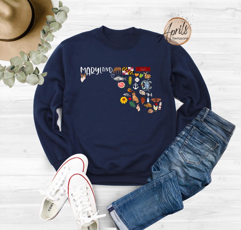 May include: Navy blue sweatshirt with a graphic of the state of Maryland, featuring various icons representing the state, including a crab, a lighthouse, and a sunflower. The text "Maryland" is printed above the graphic.