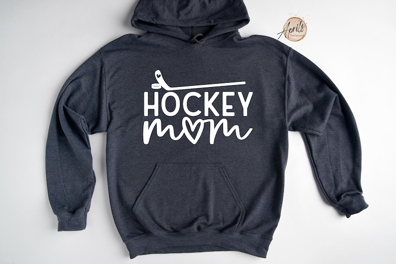 May include: A dark gray hoodie with a white graphic that says "HOCKEY mom" with a heart in the "o" of mom and a hockey stick above the text.