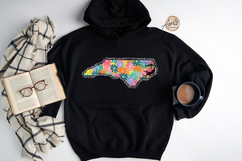 May include: Black hoodie with a floral design of the state of North Carolina. The design includes the words "In Nature's Garden, North Carolina, Heart of Carolina".