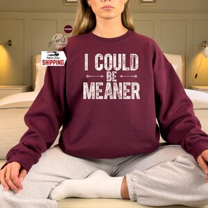 May include: A maroon sweatshirt with the text "I could be meaner" in white lettering with arrows on either side of the text.
