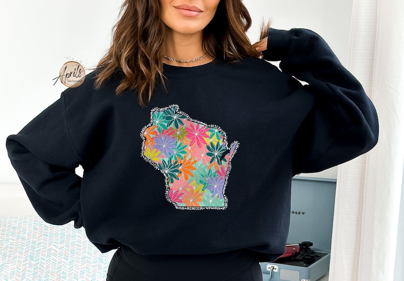 May include: Black sweatshirt with a floral design in the shape of the state of Wisconsin. The flowers are in shades of pink, orange, yellow, green, and purple.