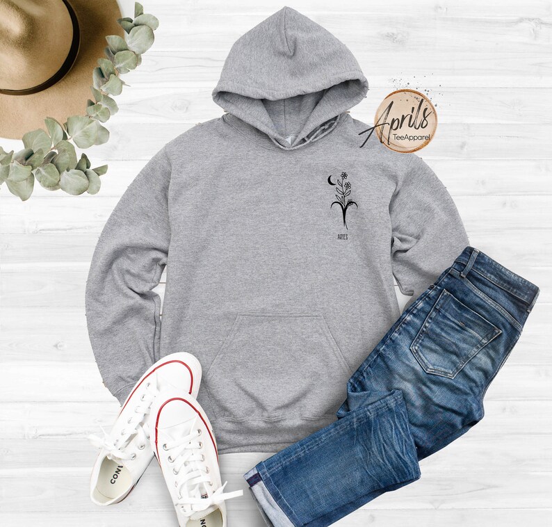 Op de afbeelding: Grijs hoodie met een zwart bloemenontwerp en de tekst "April's Tee Apparel" aan de rechterkant van de capuchon.