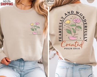 May include: Sand-colored sweatshirt with a floral design on the front and back. The front features a line drawing of a flower in a pot. The back has the text "Fearfully and Wonderfully Created" with "Psalm 139:14".