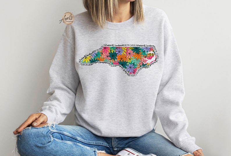 May include: A gray sweatshirt with a floral design of the state of North Carolina. The design includes the words "North Carolina" repeated around the outline of the state.