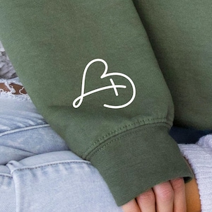 May include: A green sweatshirt with a white heart and cross design on the sleeve.