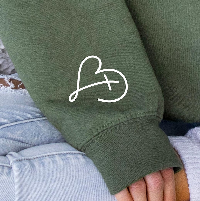 May include: A green sweatshirt with a white heart and cross design on the sleeve.