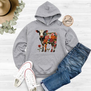 May include: Gray hooded sweatshirt with a floral cow design. The cow is black and white with colorful flowers covering its body. The text "April's Tee Apparel" is in the top right corner of the image.