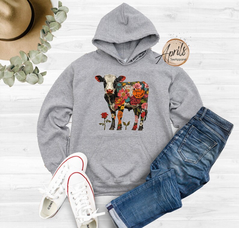 May include: Gray hooded sweatshirt with a floral cow design. The cow is black and white with colorful flowers covering its body. The text "April's Tee Apparel" is in the top right corner of the image.