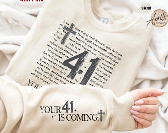 May include: Sand-colored sweatshirt with the text "4:1" and religious text printed in black. The sleeve features the text "YOUR 41+ IS COMING" with a cross. The sweatshirt is a comfortable, casual style.